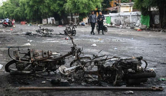 
Warga melintas di samping sepeda motor yang terbakar pascakericuhan di kawasan Kalibata, Jakarta,